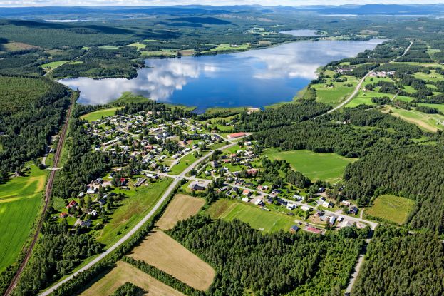 Flygbildsvy över Korsträsk i Älvsbyns kommun. Sommar med åkrar, byn och sjön Stor-korsträsket.