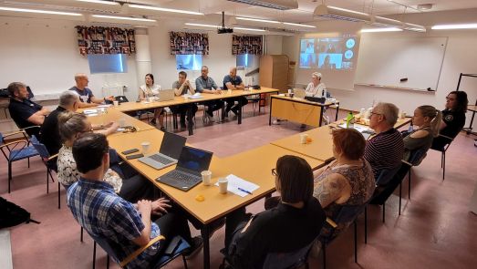Samverkansträff mellan myndigheter. På bilden sitter 15 personer vid ett bord och 6 personer deltar digitalt på en projektorduk.