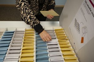 Bilden visar en person som plockar valsedlar, gul, blå och vit