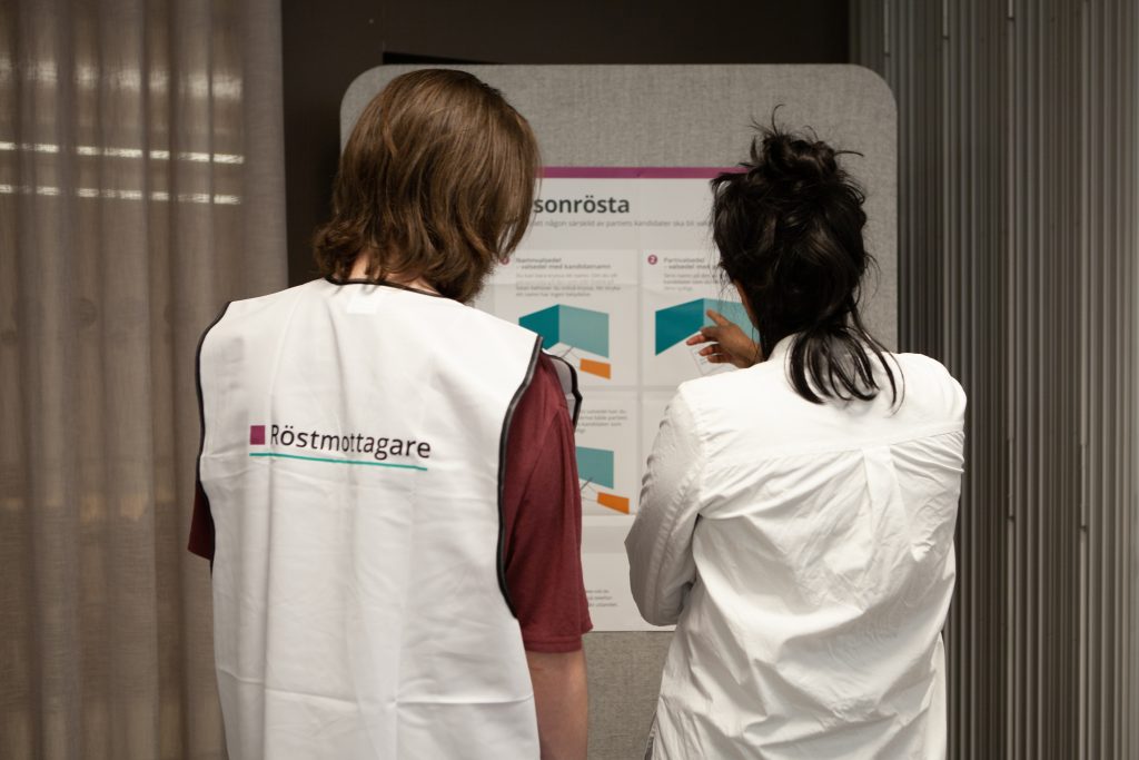 Röstmottagare som har rygger mot kameran och där det står röstmottagare på västen.