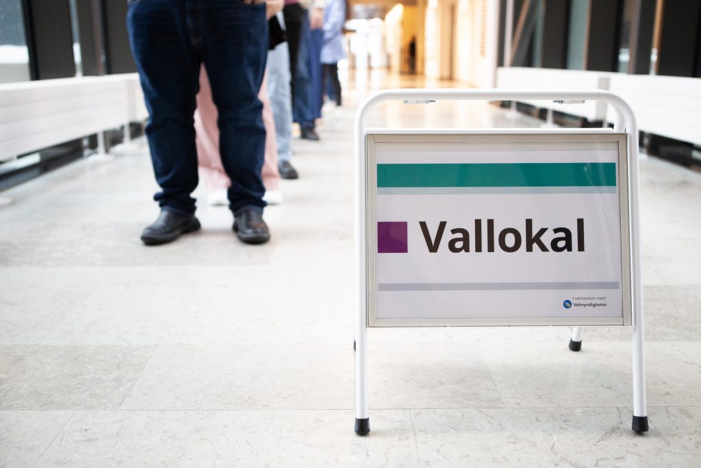 Bilden visar en skylt med text Vallokal och en kö med människor