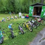 Bild på ett förråd och uppradade barncyklar på en gräsmatta.