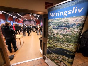Bild på en roll-up där det står näringslivs, utanför en ingång till en hall full med människor.
