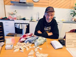 Bild på en man som sitter vid ett bord. På bordet ligger flera små triangelformade träpjäser utspridda.