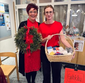 Bild på två kvinnor. Den ena kvinnan håller i en korg fylld med olika saker, den andra håller i en julkrans.