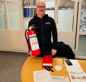 Bild på en man som står vid ett bord och håller en brandsläckare.