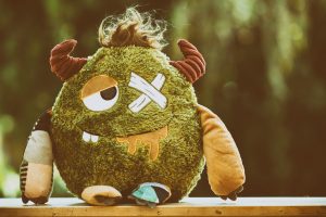 Bilden visar ett grönt gosedjurs monster med horn, hår och ett lappat öga