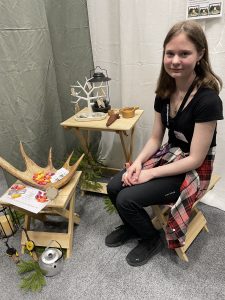 Bild på en tjej som sitter på en pall vid en monter.