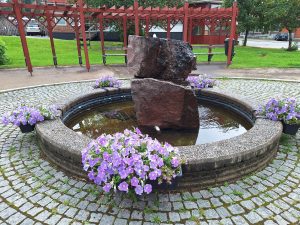 Bilden visar en mindre fontän med blommor intill sig.