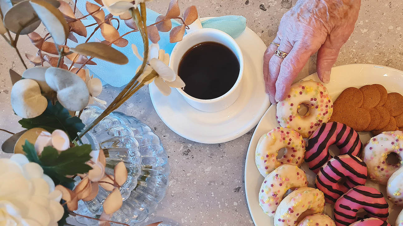 Bilden visar en hand som tar en kaka till kaffet från ett kakfat